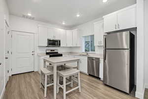Kitchen with stainless steel appliances, light wood-style floors, white cabinetry, and recessed lighting