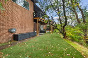 View of home's exterior featuring a patio area, a yard, brick siding, a deck, and stairway