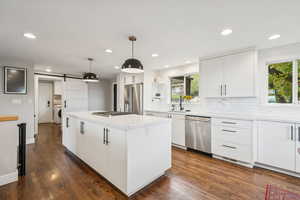 Kitchen with a barn door, white cabinetry, dark wood-style floors, a kitchen island, and recessed lighting