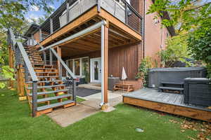 Back of house featuring a wooden deck, stairway, a patio area, a hot tub, and a yard