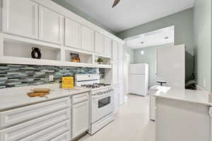 Kitchen with white cabinetry, white appliances, open shelves, light stone countertops, and hanging light fixtures