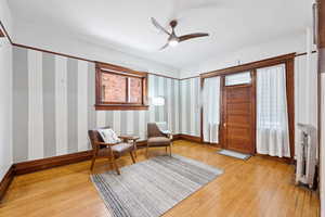 Sitting room featuring light wood-type flooring, a ceiling fan, and wallpapered walls