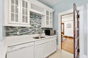 Kitchen featuring backsplash, white dishwasher, white cabinets, black microwave, and light stone counters
