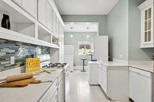 Kitchen featuring white cabinetry, white appliances, decorative backsplash, and hanging light fixtures