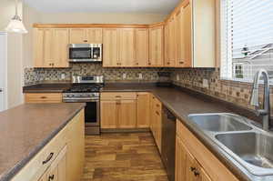 Kitchen with light brown cabinets, stainless steel appliances, dark countertops, and decorative backsplash