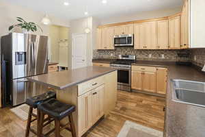 Kitchen with light brown cabinets, stainless steel appliances, tasteful backsplash, a kitchen breakfast bar, and recessed lighting