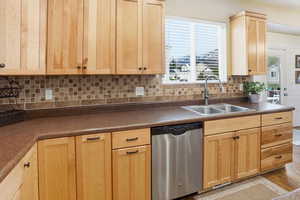Kitchen featuring light brown cabinetry, dishwasher, decorative backsplash, dark countertops, and light wood finished floors