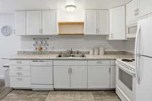Kitchen featuring white appliances, backsplash, white cabinets, and light countertops