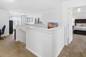 Corridor with light carpet, an upstairs landing, and an office area