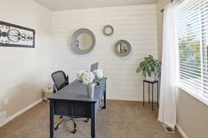 Carpeted home office featuring wood walls