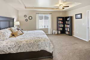 Bedroom with a tray ceiling, light colored carpet, and ceiling fan