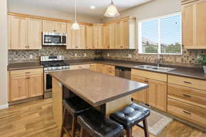 Kitchen with light brown cabinets, stainless steel appliances, dark countertops, tasteful backsplash, and recessed lighting