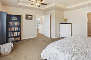 Carpeted bedroom featuring a raised ceiling and ceiling fan