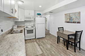 Kitchen featuring white appliances, light countertops, decorative backsplash, white cabinetry, and light wood-type flooring