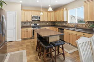 Kitchen featuring light brown cabinets, stainless steel appliances, backsplash, dark countertops, and dark wood-style flooring