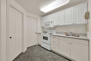Kitchen with white appliances, white cabinetry, and light countertops