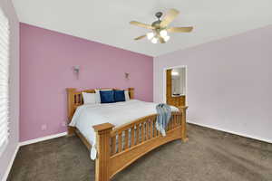 Bedroom with dark colored carpet, a ceiling fan, and connected bathroom
