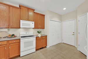 Kitchen featuring white appliances, light countertops, brown cabinets, recessed lighting, and light flooring