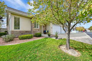 View of front of property featuring stone siding, driveway, stucco siding, a front lawn, and a shingled roof