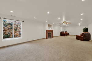 Living room with a fireplace with flush hearth, recessed lighting, light colored carpet, and ceiling fan
