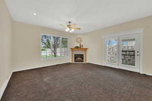 Unfurnished living room featuring dark colored carpet, a fireplace with flush hearth, and a ceiling fan