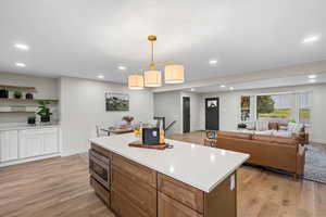Kitchen with brown cabinets, hanging light fixtures, light wood-style flooring, recessed lighting, and stainless steel microwave
