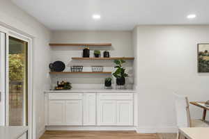 Bar area featuring white cabinetry, light wood-style flooring, open shelves, light stone countertops, and recessed lighting