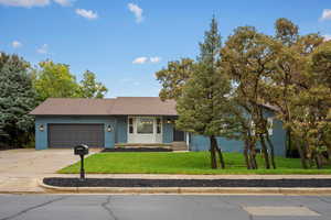 View of front facade with a front lawn, brick siding, concrete driveway, covered porch, and an attached garage