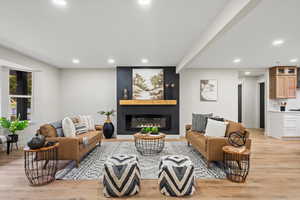 Living room with recessed lighting, light wood-type flooring, a large fireplace, and beamed ceiling
