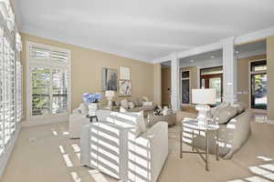 Carpeted living area featuring ornate columns and crown molding