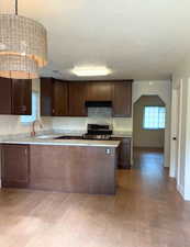 Kitchen featuring dark brown cabinetry, decorative light fixtures, stainless steel range with gas cooktop, a peninsula, and a textured ceiling