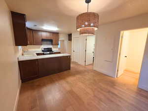 Kitchen with a textured ceiling, a peninsula, light wood-style floors, stainless steel gas range, and decorative light fixtures