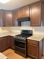 Kitchen featuring range with two ovens, light stone counters, light wood-style flooring, under cabinet range hood, and a textured ceiling