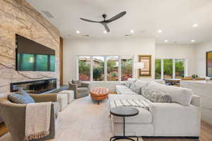 Living room featuring a stone fireplace, plenty of natural light, wood finished floors, recessed lighting, and a ceiling fan