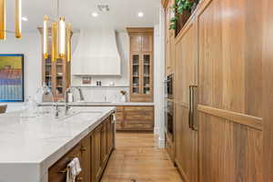 Kitchen with decorative light fixtures, brown cabinetry, light stone countertops, light wood-style floors, and recessed lighting