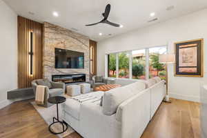 Living room featuring light wood-type flooring, a ceiling fan, a large fireplace, and recessed lighting