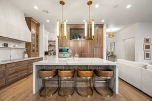 Kitchen featuring glass insert cabinets, open shelves, brown cabinets, light stone counters, and recessed lighting