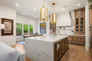 Kitchen featuring light stone countertops, light wood-style flooring, recessed lighting, a center island with sink, and glass insert cabinets