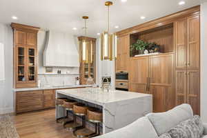 Kitchen featuring a breakfast bar, open shelves, light stone counters, custom exhaust hood, and hanging light fixtures
