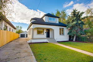 Bungalow-style home with a detached garage, roof with shingles, an outdoor structure, covered porch, and brick siding