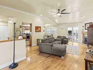Living area featuring ornamental molding, light wood floors, a gas fireplace with flush hearth, ceiling fan, and vaulted ceiling.