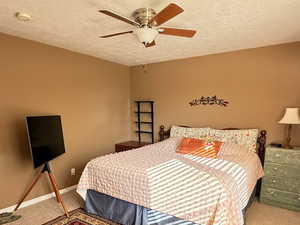 Carpeted bedroom featuring a textured ceiling and ceiling fan
