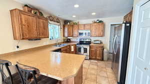 Kitchen featuring stainless steel appliances, a breakfast bar, a peninsula, brown cabinets, and a textured ceiling