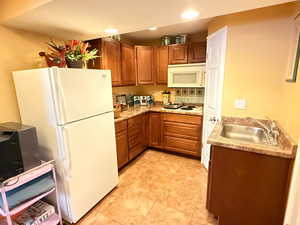 Kitchen with brown cabinets, white appliances, light countertops, and recessed lighting