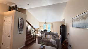 Living room featuring vaulted ceiling, dark wood-type flooring, a chandelier, stairway, and a textured ceiling