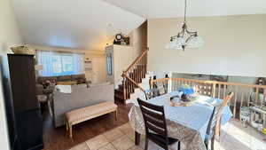 Dining space featuring a chandelier, light tile patterned floors, high vaulted ceiling, and stairs