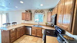 Kitchen featuring brown cabinets, stainless steel appliances, a textured ceiling, recessed lighting, and a kitchen breakfast bar