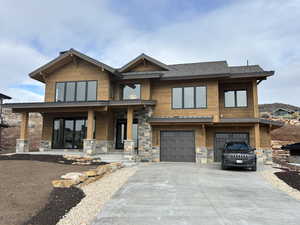 View of front facade featuring an attached garage, driveway, covered porch, and stone siding