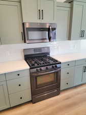 Kitchen with appliances with stainless steel finishes, light wood-type flooring, decorative backsplash, and gray cabinets