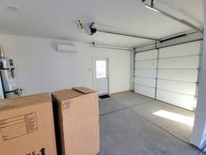 Garage with secured water heater, washing machine and dryer, fridge, a wall mounted air conditioner, and a garage door opener
